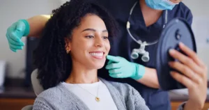 A woman smiles at the mirror at the dentist after receiving a deep cleaning