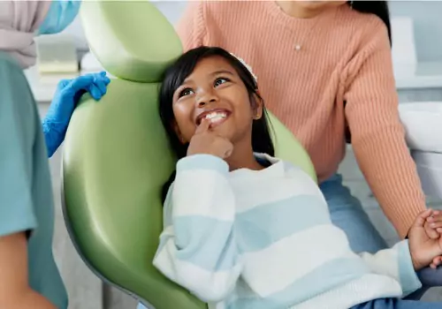 A young girl smiling and pointing at her clean teeth, showing her Pediatric Dentist in Peoria IL