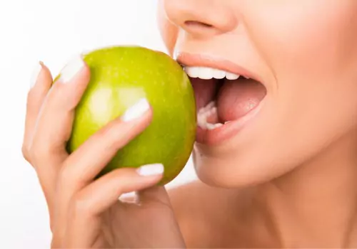 A woman is seen biting into an apple. The Smile Center is a holistic dental office in Peoria IL.