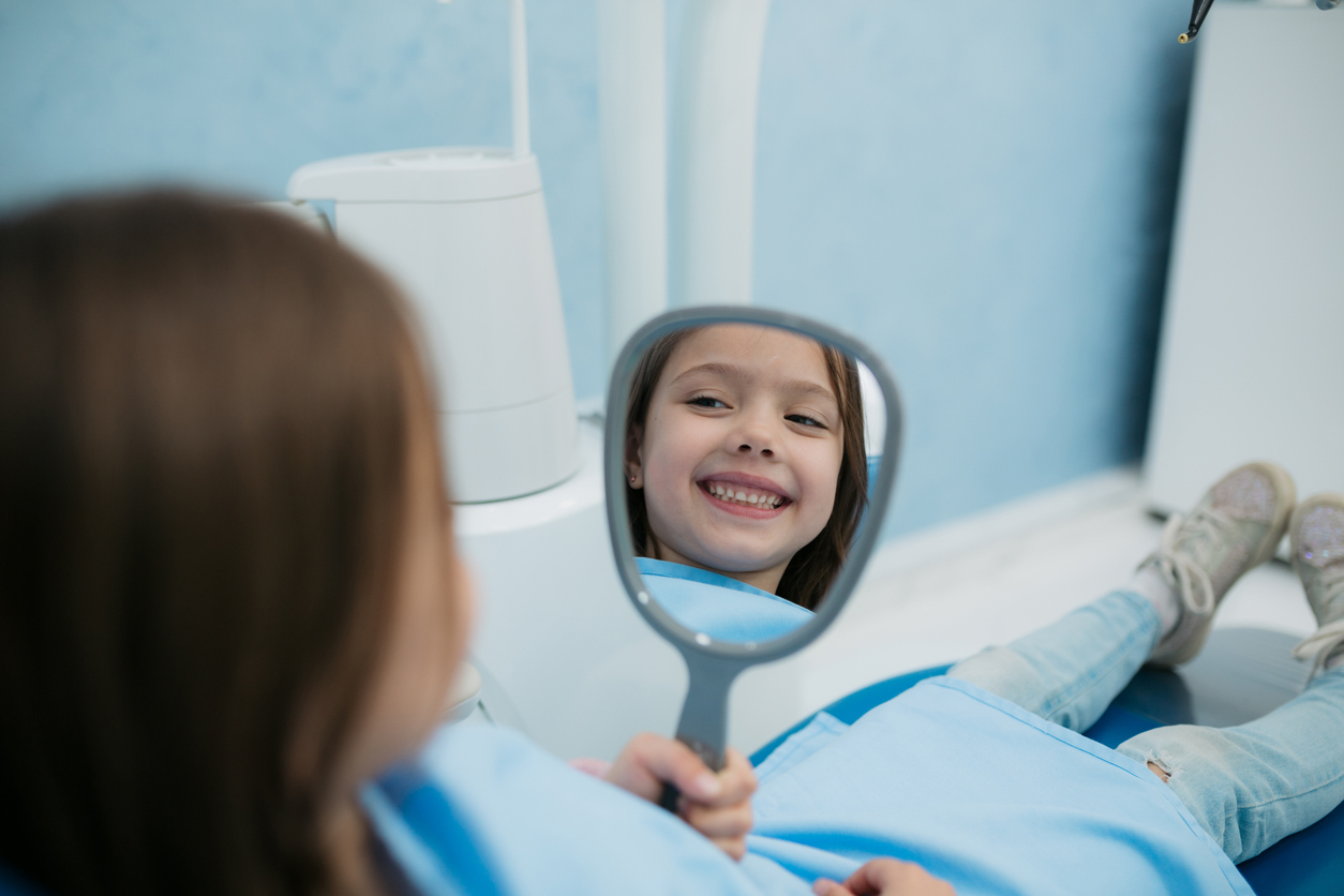 A happy girl looks in the mirror after a great appointment at the Smile Center of Peoria IL
